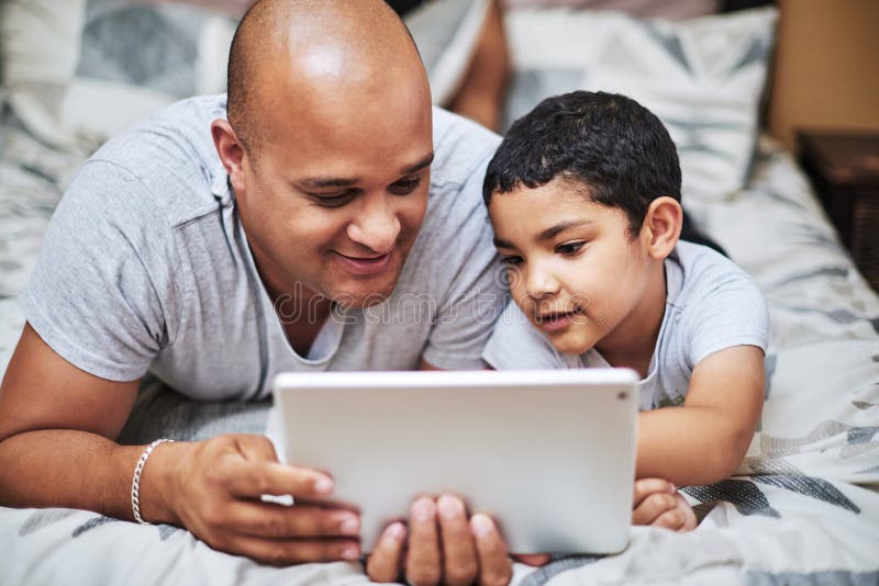 I wonder what will happen next. a cheerful young man and his son watching videos on a digital tablet together while