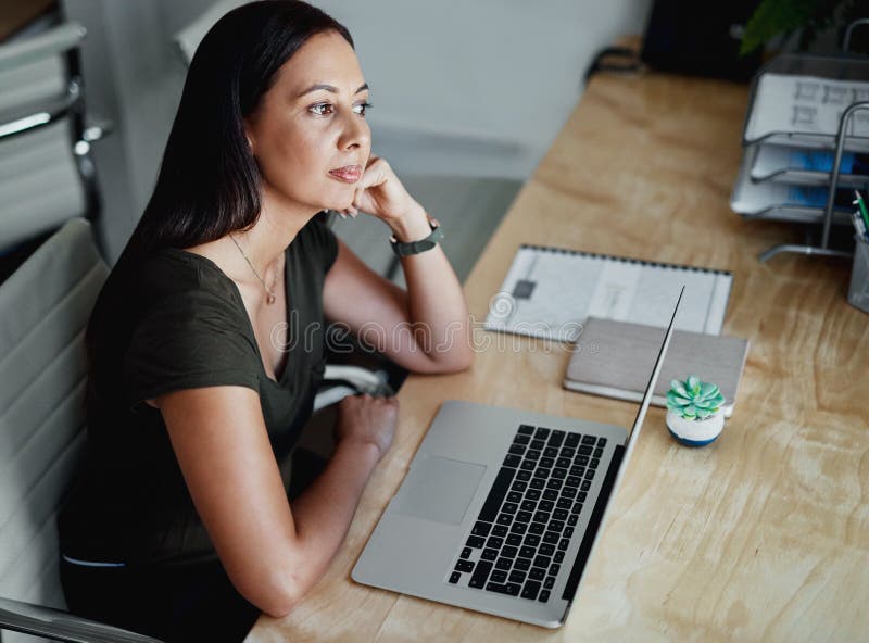 I wonder which task I should do first. an attractive young businesswoman sitting alone and looking contemplative in her