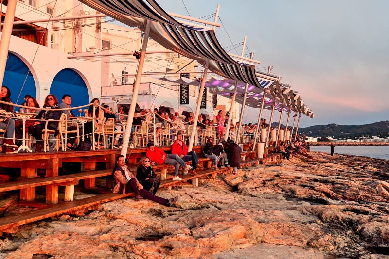 Ibiza Island, Spain - May 1, 2018: Crowds of people meet the sunset at the seafront terrace of Cafe Del Mar. This place is famous for views to the sunsets and lounge music. Ibiza, Balearic Islands. Spain. Ibiza Island, Spain - May 1, 2018: Crowds of people meet the sunset at the seafront terrace of Cafe Del Mar. This place is famous for views to the sunsets and lounge music. Ibiza, Balearic Islands. Spain