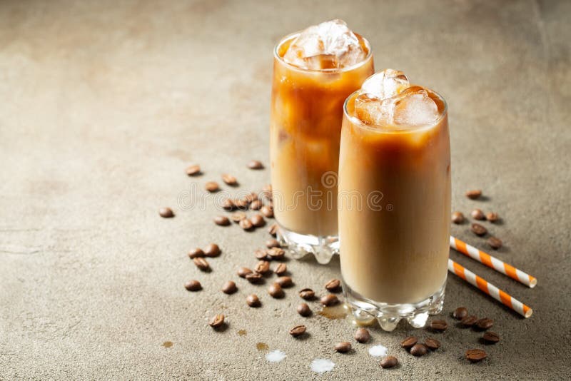 Ice coffee in a tall glass with cream poured over and coffee beans. Cold summer drink on a brown rusty background with
