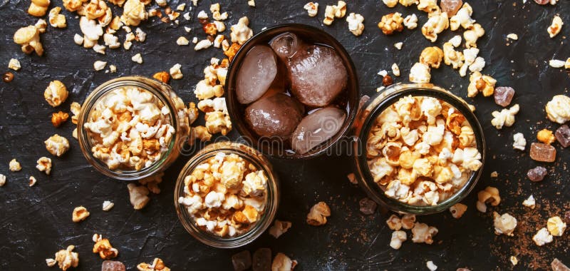 Ice cola and caramel popcorn, unhealthy food and drink, black table, top view.