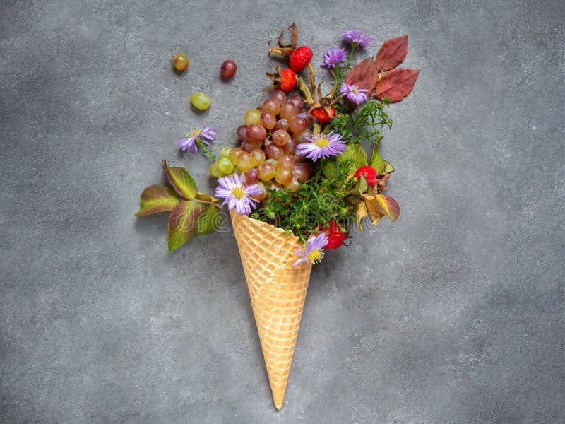 Ice cream cone with autumn leaves, rose hips and flowers on a gray background. Greeting card. Conceptual photo - gifts of autumn.