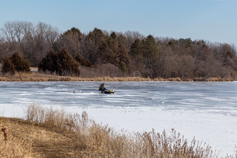 Ice fishing; frozen lake surface in winter with ice fisherman tending his stuff on the lake.