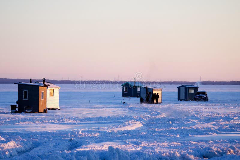 Ice fishing huts and a car on a frozen lake.