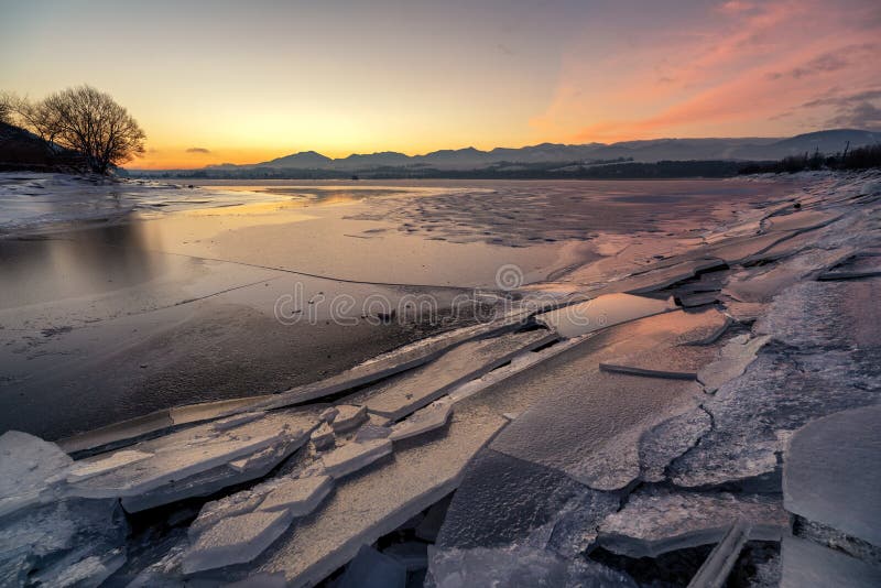 Ľadové kryhy na brehu jazera. Farebná obloha pri východe slnka za chladného zimného rána. Priehrada Liptovská Mara, Slovensko