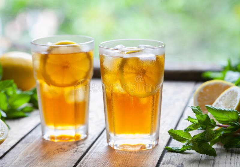 Ice tea with lemon slices and mint on wooden table with a view to the terrace. Close up summer beverage