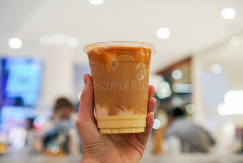 Iced salted egg Thai tea. Hand holding a plastic cup of Thai tea with salted egg sauce and milk pudding. Blurred background
