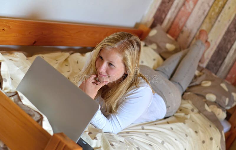 I very love my work place - says a blonde young woman working on laptop in her bed. I very love my work place - says a blonde young woman working on laptop in her bed