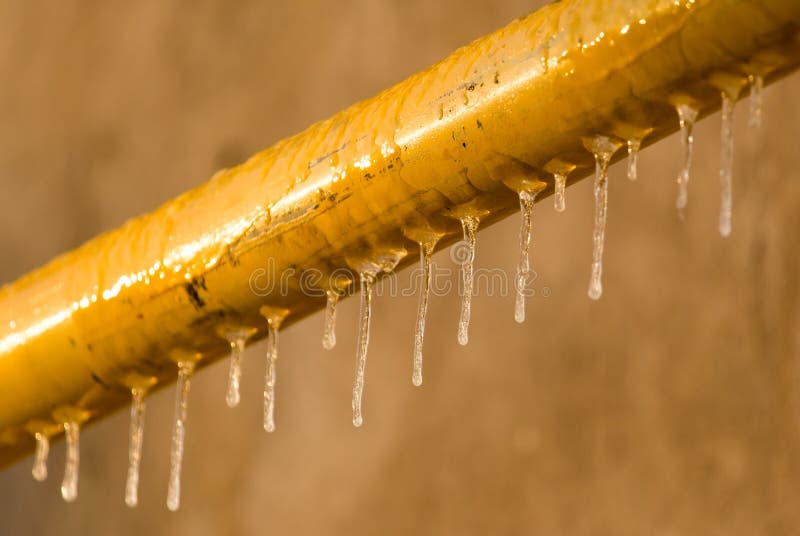 Icicles on a yellow pipe at sunset stock photo