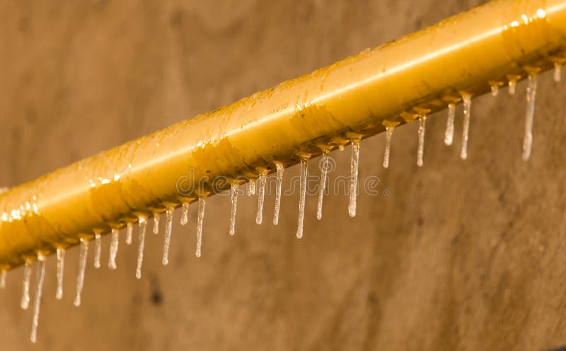 Icicles on a yellow pipe at sunset royalty free stock photo