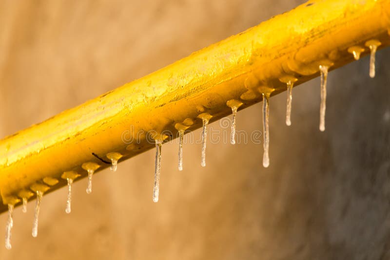 Icicles on a yellow pipe at sunset royalty free stock photo