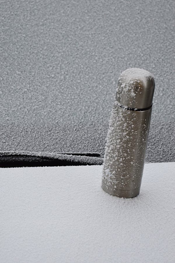 Icing covered steel thermos bottle placed on frozen trunk of a car, front window of a car in background.