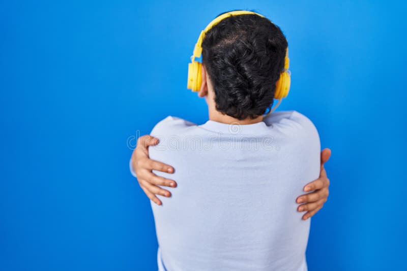 Icke-binär person som lyssnar på musik med hörlurar som kramar sig själv, glad och positiv bakifrån arkivfoton