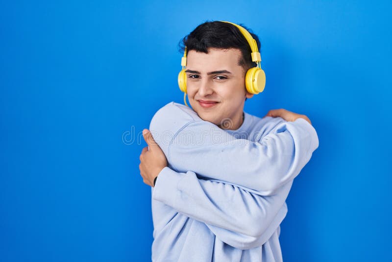 Icke-binär person som lyssnar på musik med hörlurar som kramar sig själv, glad och positiv, leende självsäker fotografering för bildbyråer