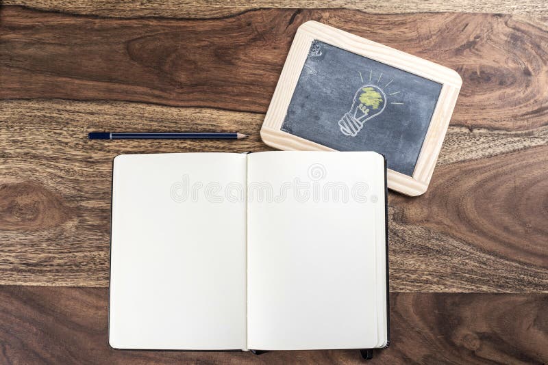 Open plain empty page notebook with pencil and light bulb on blackboard on rustic wood table. Open plain empty page notebook with pencil and light bulb on blackboard on rustic wood table