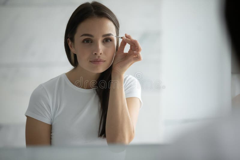 Concentrated young female doing sharp accurate eyebrow contours using tweezer royalty free stock photos