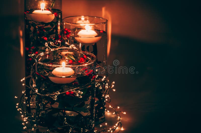 Ideas creativas con plantas de velas y jarrón lleno del concepto de navidad de agua. Velas encendidas flotando en el agua en un jarrón lleno de agua y flores de colores en un fondo oscuro con pequeñas luces brillantes