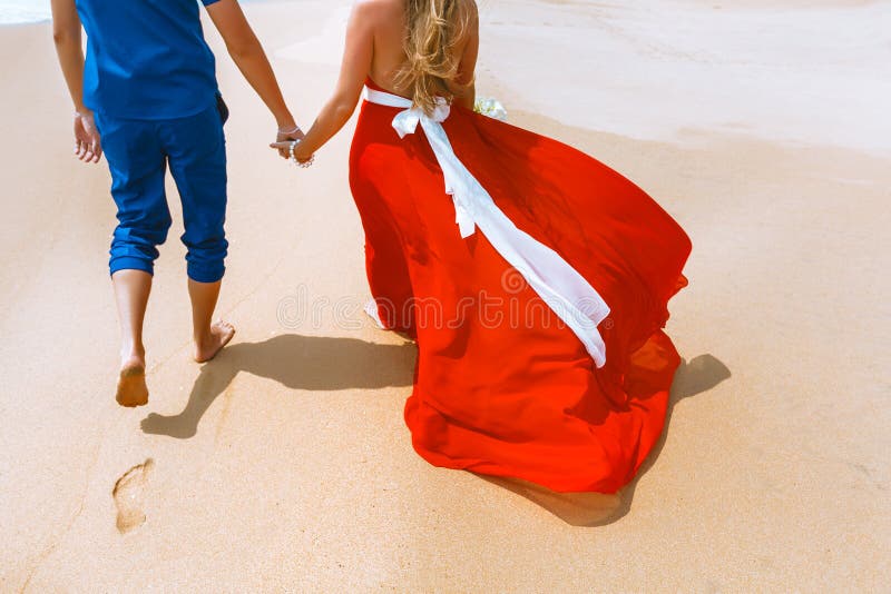 Ideia traseira dos pares loving que andam afastado com pegadas no Sandy Beach Irmãs que prendem as mãos imagem de stock royalty free Ideia traseira dos pares loving que andam afastado com pegadas no Sandy Beach Irmãs que prendem as mãos imagem de stock royalty free