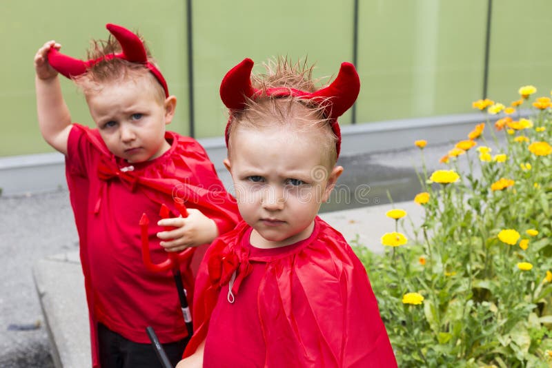 Identical toddler twin disguised as devil scowling with brother in soft focus background stock photos Identical toddler twin disguised as devil scowling with brother in soft focus background stock photos