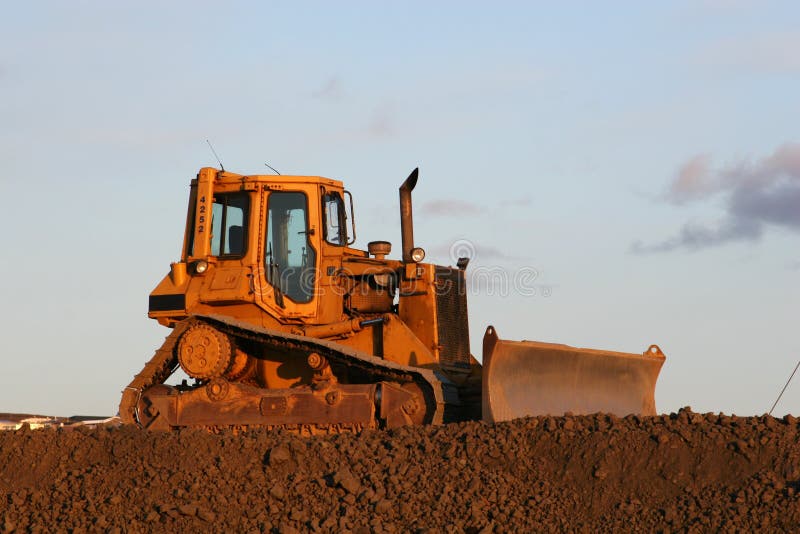 A big yellow bulldozer standing on a crest against the sky. A big yellow bulldozer standing on a crest against the sky