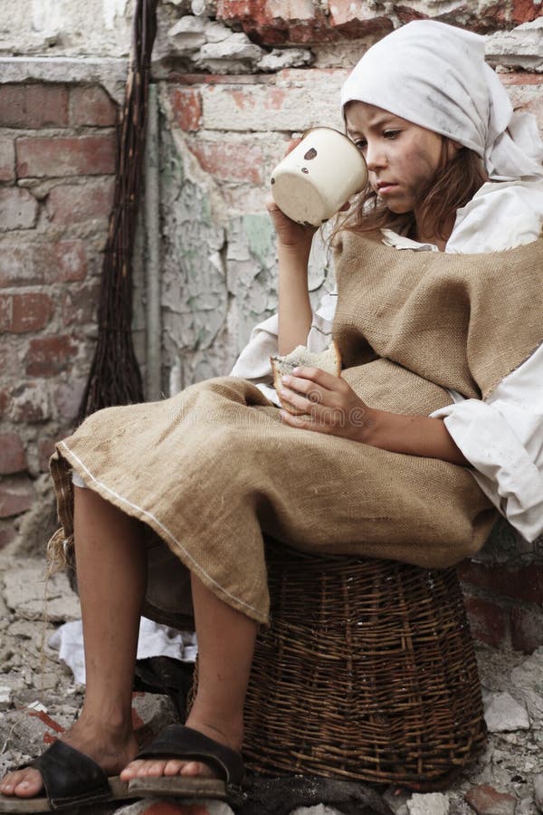 Hungry child wearing dirty clothes, piece of bread and a vintage mug in her hands. More available. Hungry child wearing dirty clothes, piece of bread and a vintage mug in her hands. More available.