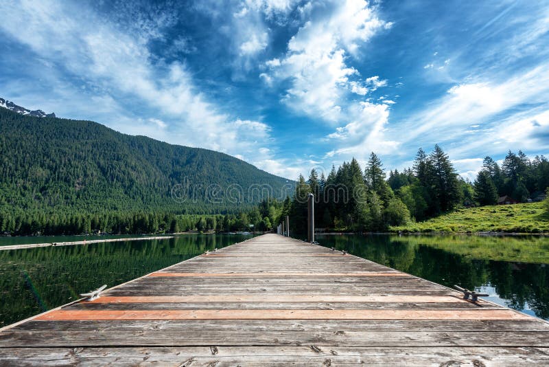 Idyllische Aussicht auf einen Holzsteg im See mit üppig bewaldetem Berg lizenzfreie stockbilder