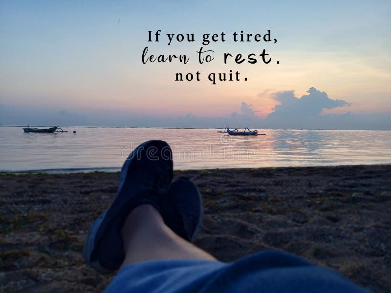 Inspirational motivational quote - If you get tired, learn to rest, not quit. With blurry image of young woman legs sitting alone. On sands, relax and enjoying the morning sunrise light view over the sea. Recharge time concept. Inspirational motivational quote - If you get tired, learn to rest, not quit. With blurry image of young woman legs sitting alone. On sands, relax and enjoying the morning sunrise light view over the sea. Recharge time concept