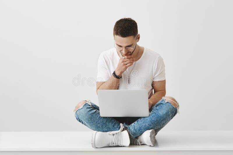 Idérikt freelancer- och studentarbete Studioskott av den attraktiva moderna mannen i exponeringsglas som sitter med korsade ben p arkivfoton Idérikt freelancer- och studentarbete Studioskott av den attraktiva moderna mannen i exponeringsglas som sitter med korsade ben p arkivfoton