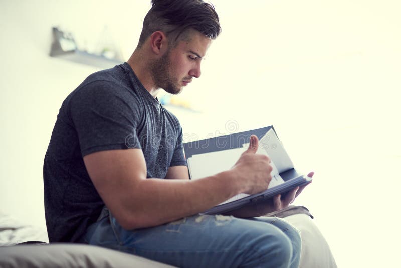 If you want it, youll work for it. a confident young man studying some paperwork while sitting on his bed at home. stock photography