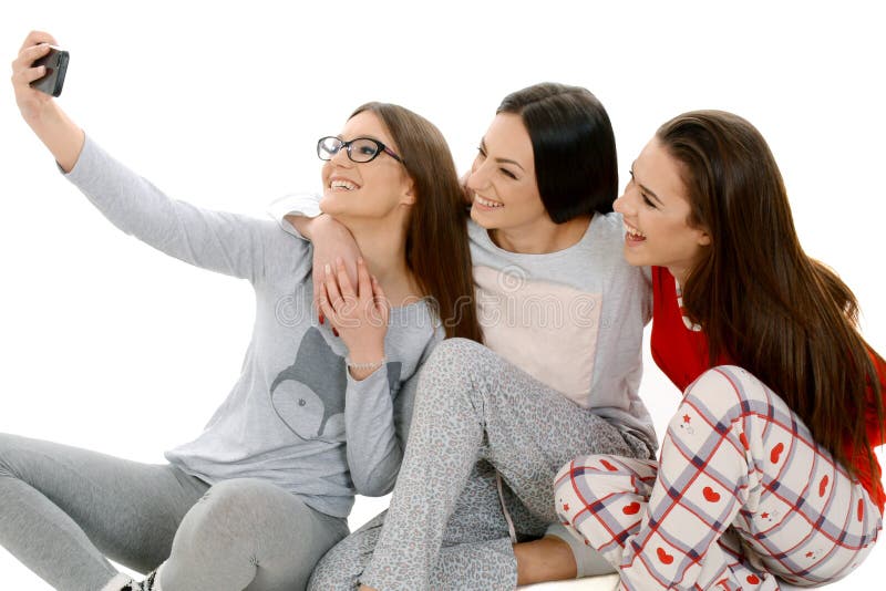 Three beautiful happy girls ih their pajamas taking selfie with smartphone. friendship, people and pajama party concept - happy friends or teenage girls having fun. Three beautiful happy girls ih their pajamas taking selfie with smartphone. friendship, people and pajama party concept - happy friends or teenage girls having fun.