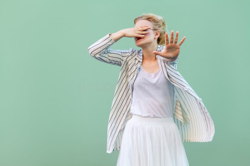 Ik wil niet dit bekijken Doen schrikken jonge blondevrouw in wit overhemd, rok, en gestreepte blouse status, die haar ogen behand stock foto Ik wil niet dit bekijken Doen schrikken jonge blondevrouw in wit overhemd, rok, en gestreepte blouse status, die haar ogen behand stock foto