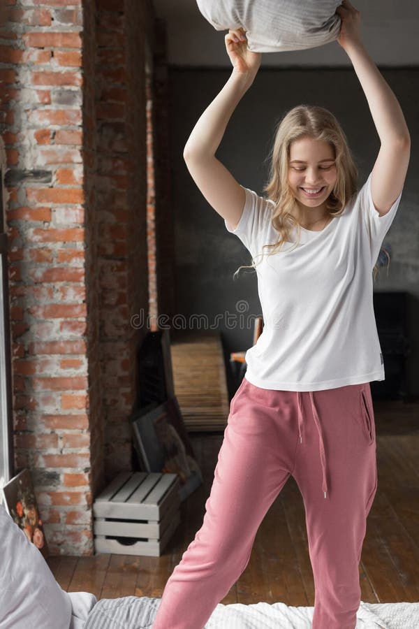 Iklädd pajama för gullig flicka på en säng med en kudde, le och en kuddestridighet arkivbild Iklädd pajama för gullig flicka på en säng med en kudde, le och en kuddestridighet arkivbild