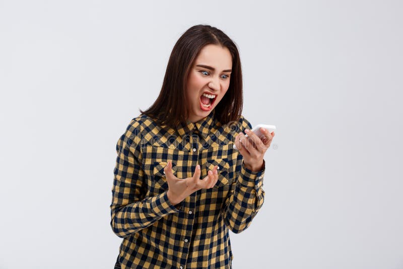 Angry young beautiful girl in plaid shirt screaming at phone over white background. Copy space. Angry young beautiful girl in plaid shirt screaming at phone over white background. Copy space.