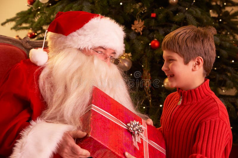 Il Babbo Natale che dà regalo al ragazzo davanti a Christm fotografie stock Il Babbo Natale che dà regalo al ragazzo davanti a Christm fotografie stock