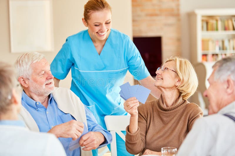 Smiling caregiver is watching at the card game of a senior citizen group in retirement home. Smiling caregiver is watching at the card game of a senior citizen group in retirement home