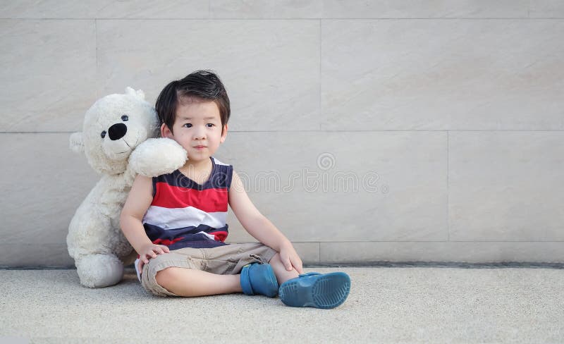Il bambino asiatico del primo piano con l'orso che la bambola si siede alla via sulla parete di pietra di marmo ha strutturato il fotografie stock Il bambino asiatico del primo piano con l'orso che la bambola si siede alla via sulla parete di pietra di marmo ha strutturato il fotografie stock