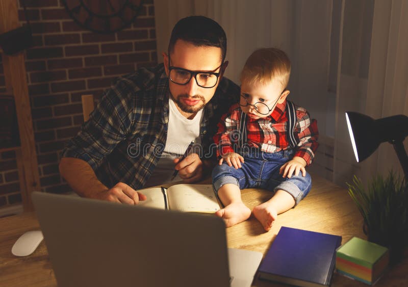Il bambino del figlio e del padre lavora a casa al computer nello scuro fotografie stock libere da diritti Il bambino del figlio e del padre lavora a casa al computer nello scuro fotografie stock libere da diritti