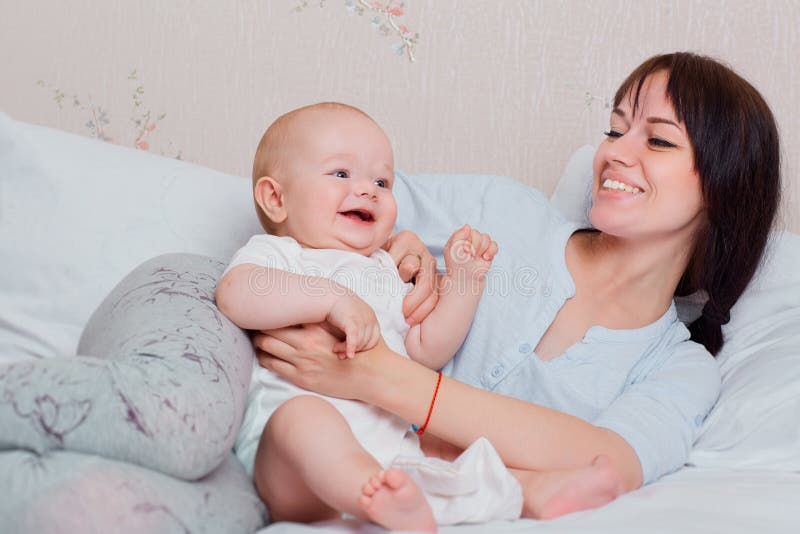 Il bambino felice gioca con la mummia in pigiami sul letto, sulla risata e sul MP fotografia stock Il bambino felice gioca con la mummia in pigiami sul letto, sulla risata e sul MP fotografia stock