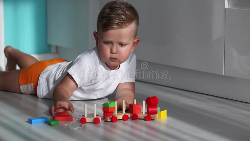 Il bambino mette un treno a partire da blocchi geometrici. il ragazzo giace per due anni sul pavimento e gioca con un treno di imp video d archivio