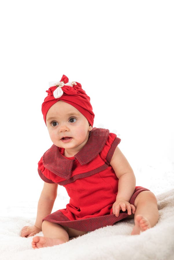 Il bambino piccolo si è vestito in vestiti rossi che si siedono sulla coperta contro il fondo bianco fotografia stock Il bambino piccolo si è vestito in vestiti rossi che si siedono sulla coperta contro il fondo bianco fotografia stock