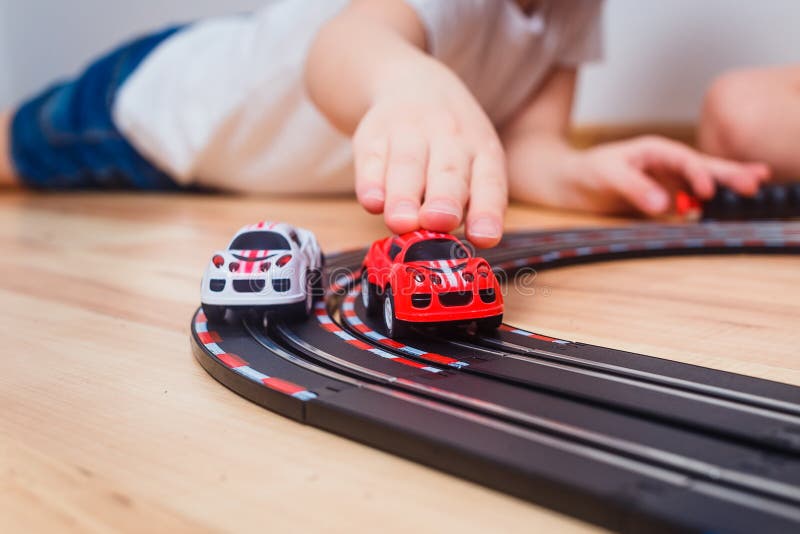 Il bambino rotola le piccole automobili su una pista dell'automobile del giocattolo immagine stock Il bambino rotola le piccole automobili su una pista dell'automobile del giocattolo immagine stock