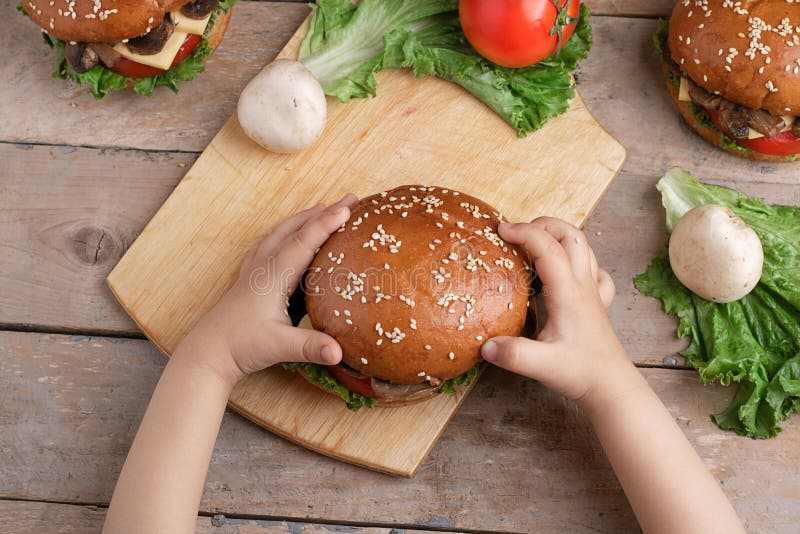 Il bambino tiene l'hamburger del fungo, verdure crude intorno fotografia stock Il bambino tiene l'hamburger del fungo, verdure crude intorno fotografia stock