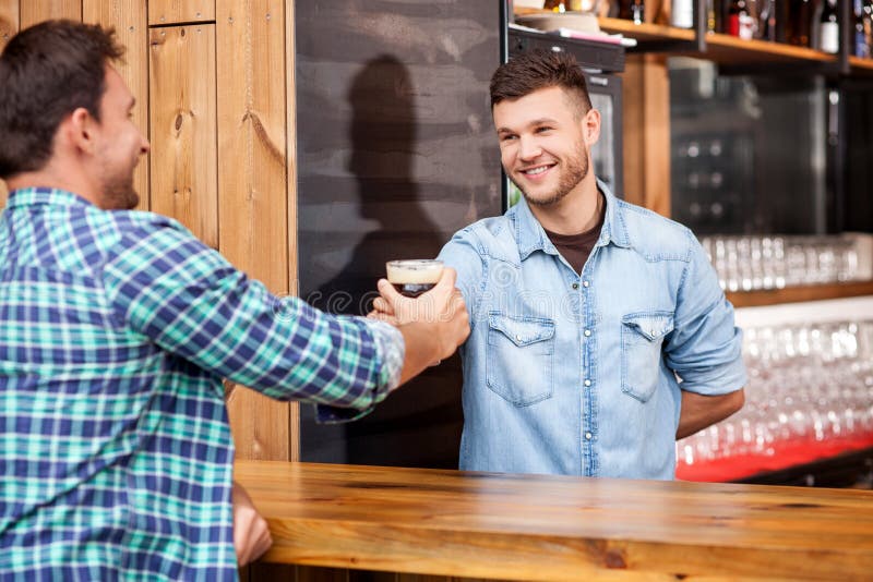 Il barista bello sta servendo il suo cliente nella barra fotografia stock libera da diritti Il barista bello sta servendo il suo cliente nella barra fotografia stock libera da diritti