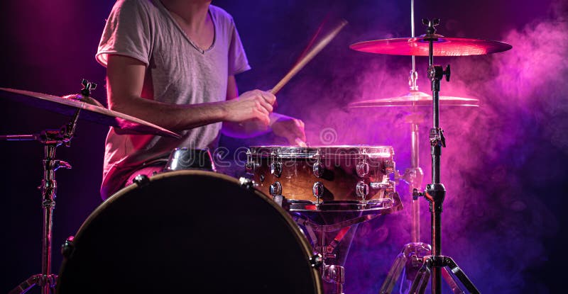 The drummer plays the drums. Beautiful blue and red background, with rays of light. Beautiful special effects smoke and lighting. The process of playing a musical instrument. The concept of music. The drummer plays the drums. Beautiful blue and red background, with rays of light. Beautiful special effects smoke and lighting. The process of playing a musical instrument. The concept of music