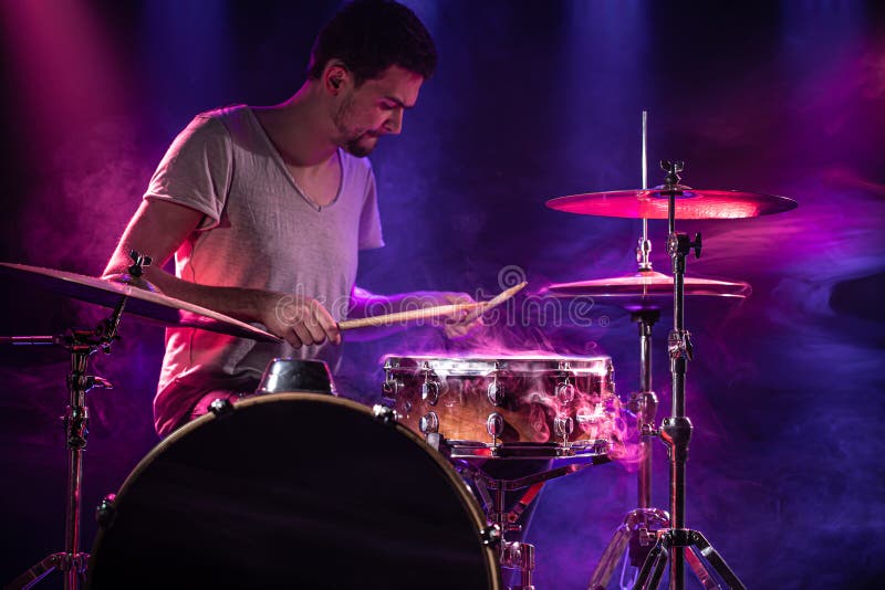 The drummer plays the drums. Beautiful blue and red background, with rays of light. Beautiful special effects smoke and lighting. The process of playing a musical instrument. The concept of music. The drummer plays the drums. Beautiful blue and red background, with rays of light. Beautiful special effects smoke and lighting. The process of playing a musical instrument. The concept of music