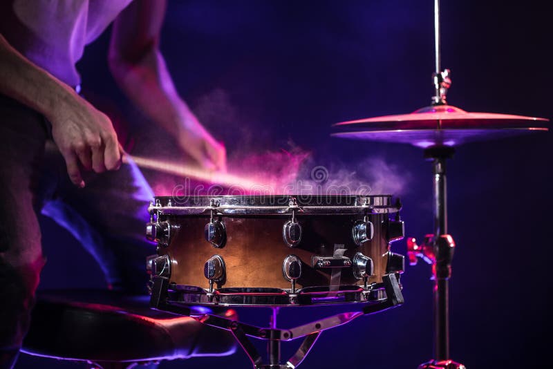 The drummer plays the drums. Beautiful blue and red background, with rays of light. Beautiful special effects smoke and lighting. The process of playing a musical instrument. The concept of music. The drummer plays the drums. Beautiful blue and red background, with rays of light. Beautiful special effects smoke and lighting. The process of playing a musical instrument. The concept of music