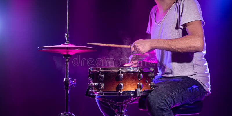 The drummer plays the drums. Beautiful blue and red background, with rays of light. Beautiful special effects smoke and lighting. The process of playing a musical instrument. The concept of music. The drummer plays the drums. Beautiful blue and red background, with rays of light. Beautiful special effects smoke and lighting. The process of playing a musical instrument. The concept of music