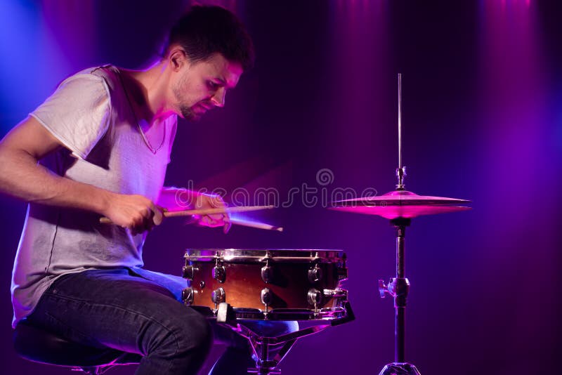 The drummer plays the drums. Beautiful blue and red background, with rays of light. Beautiful special effects smoke and lighting. The process of playing a musical instrument. The concept of music. The drummer plays the drums. Beautiful blue and red background, with rays of light. Beautiful special effects smoke and lighting. The process of playing a musical instrument. The concept of music