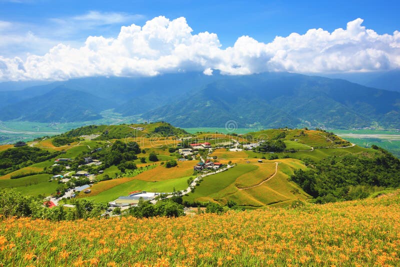 Il bello paesaggio dell'emerocallide fiorisce con il villaggio e le montagne fotografia stock libera da diritti Il bello paesaggio dell'emerocallide fiorisce con il villaggio e le montagne fotografia stock libera da diritti