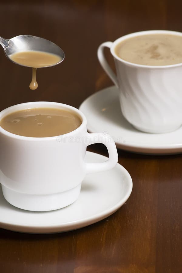 Two coffee cups. one coffee cup has a spoon being removed and the coffee dripping off the spoon. Two coffee cups. one coffee cup has a spoon being removed and the coffee dripping off the spoon.